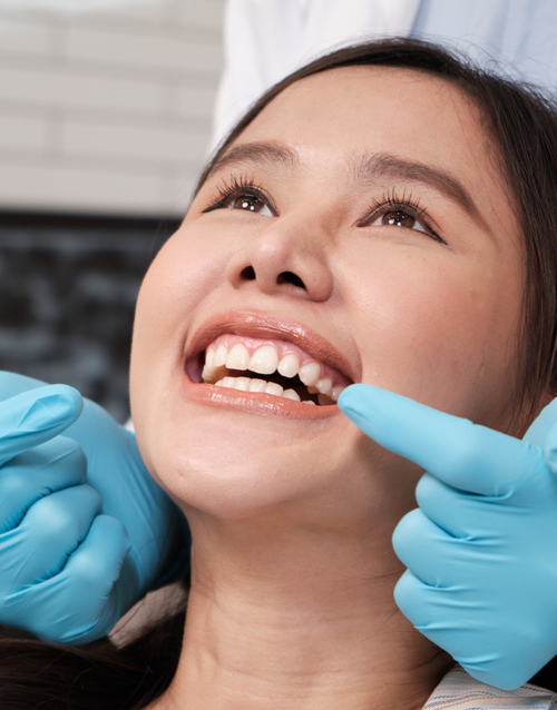 Dentist wearing blue gloves showing dentures to patient explaining with dental probe during consultation in dental clinic